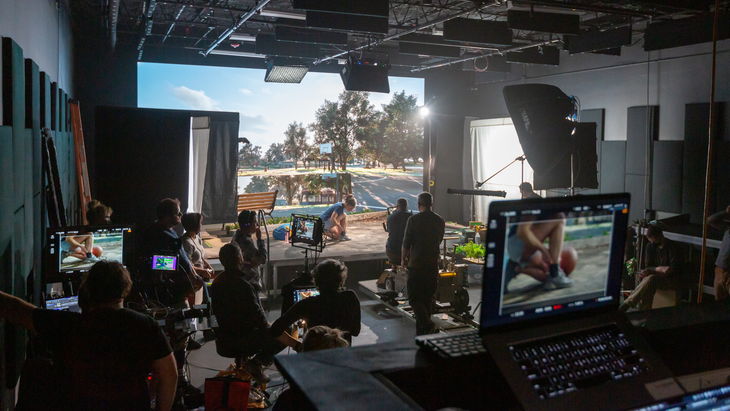 A film crew records a basketball scene on a virtual production set, with multiple monitors showing the live feed.