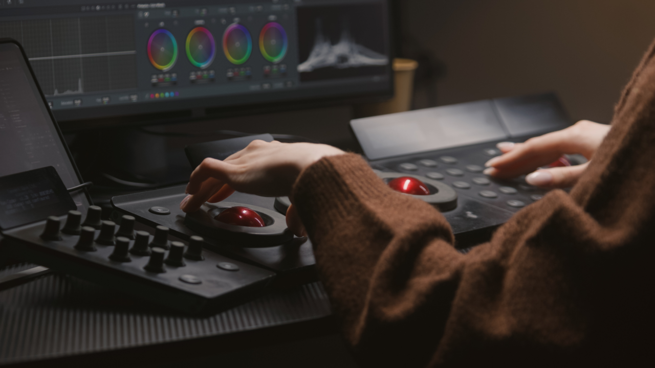 A person operates a professional color grading control panel, adjusting color wheels displayed on a monitor.