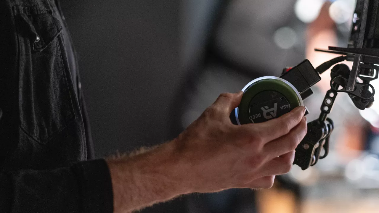 A close-up shot of a hand adjusting the focus on a camera lens during a production shoot.